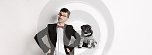 Animals, party and celebration concept. Handsome young man and puppy in formal suits looking at camera, standing over