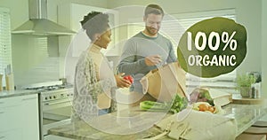 Animation of 100 percent organic text over diverse couple preparing healthy meal in kitchen