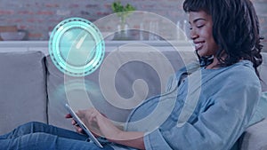 Animation of clock over biracial pregnant woman using tablet