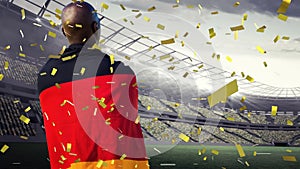 Animation of confetti floating over back of african american man in german flag at stadium