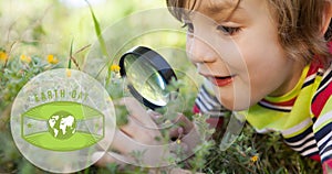 Animation of earth day text and globe logo over happy boy in nature using magnifying glass