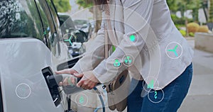 Animation of eco icons over caucasian woman charging electric car