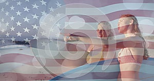 Animation of flag of usa over happy caucasian women with surfboards on beach in summer