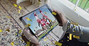 Animation of gold confetti falling over biracial man watching football on tablet