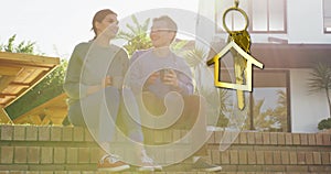 Animation of gold house key and key fob over diverse couple drinking tea at new home