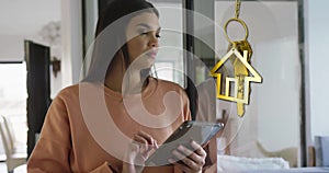 Animation of gold house key and key fob over happy biracial woman using tablet at home
