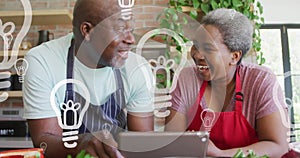 Animation of happy african american couple using tablet over lightbulbs