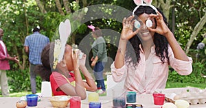 Animation of happy african american mother and daughter painting easter eggs outdoors, having fun