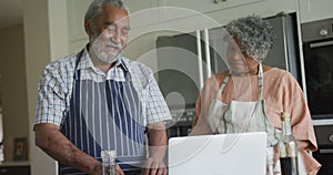 Animation of happy african american senior couple cooking together, using laptop