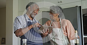 Animation of happy african american senior couple cooking together, using tablet