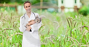 Animation of happy caucasian female vet holding yorkshire terrier pet dog, over grasses in garden