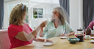 Animation of happy diverse female senior friends drinking coffee at home