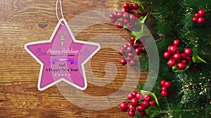 Animation of happy holidays christmas text on star shape tag over decorations on wooden background