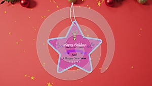 Animation of happy holidays christmas text on star tag over decorations on red background