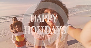 Animation of happy holidays text over african american family on the beach