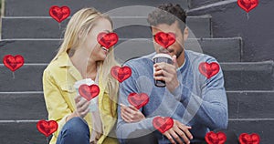 Animation of heart icons floating over happy caucasian couple talking and drinking takeaway coffee