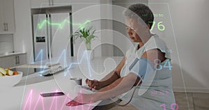 Animation of heart rate monitor over african american senior woman checking blood pressure at home