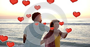 Animation of hearts moving over diverse couple in love dancing on beach in summer