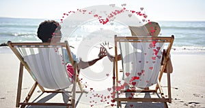 Animation of hearts moving over diverse couple in love in deckchairs on beach in summer