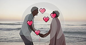 Animation of hearts moving over diverse couple in love holding hands on beach in summer