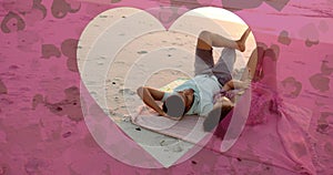 Animation of hearts moving over diverse couple in love lying on beach in summer