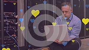 Animation of hearts over caucasian businessman using laptop in server room