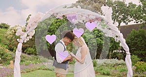 Animation of lilac hearts and happy diverse couple holding hands under wedding arch in garden