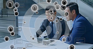 Animation of multiple profile icons over two diverse businessmen discussing over a laptop at office