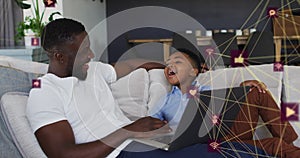 Animation of network of connections over happy african american father and son using laptop