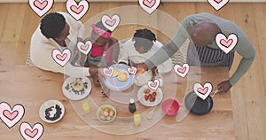 Animation of pink hearts over happy african american grandparents and grandchildren cooking at home