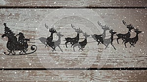 Animation of silhouette of santa claus in sleigh being pulled by reindeer on wooden rustic backgroun