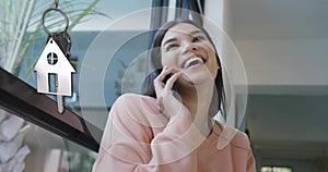 Animation of silver house key and key fob over happy biracial woman talking on the phone