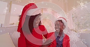 Animation of snow falling over smiling mother and daugher with santa hats waving hands