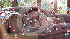 Animation of social media icons over asian woman using tablet on sofa