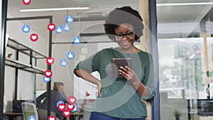 Animation of social media icons over happy african american woman using tablet in office