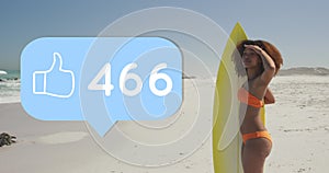 Animation of speech bubble with thumbs up digital icon and numbers, woman with surfboard on beach