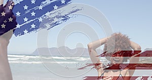 Animation of usa flag design against african american man taking pictures of his wife at the beach