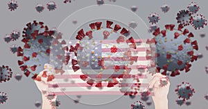 Animation of virus cells and covid icons over hands holding flag of usa