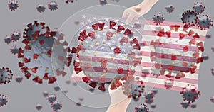 Animation of virus cells and covid icons over hands holding flag of usa