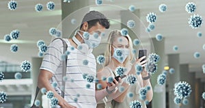 Animation of virus cells over aucasian couple wearing face masks using smartphones