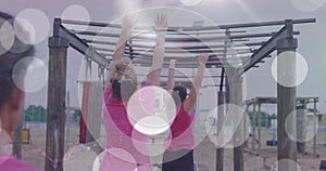 Animation of white light spots and padlock over diverse women on monkey bars at boot camp training