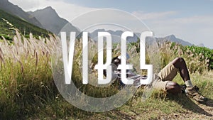 Animation of the word vibes written in white over man hiking in mountains lying in tall grass