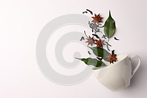 Anise stars, dry tea, green leaves and cup on white background, flat lay. Space for text