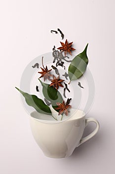 Anise stars, dry tea and green leaves falling into cup on white background, flat lay