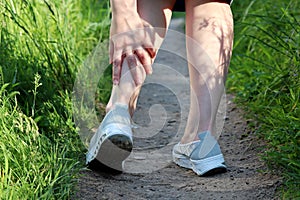 Ankle sprain, woman grabbed her leg while walking on a meadow