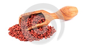 Annatto seeds in wooden scoop, isolated on white background. Achiote seeds, bixa orellana. Natural dye for cooking and food. Close
