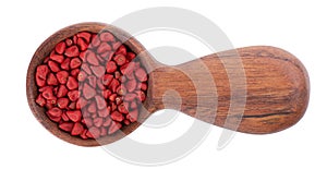 Annatto seeds in wooden spoon, isolated on a white background. Achiote seeds, bixa orellana. Natural dye for cooking and