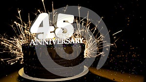 Anniversary 45 greeting card. Chocolate cake decorated with colored dragees with white numbers on a wooden table with fireworks in