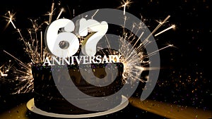 Anniversary 67 greeting card. Chocolate cake decorated with colored dragees with white numbers on a wooden table with fireworks in