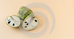 Annona cherimola. Whole custard apple and a halved custard apple on a cream-coloured background. Copy space